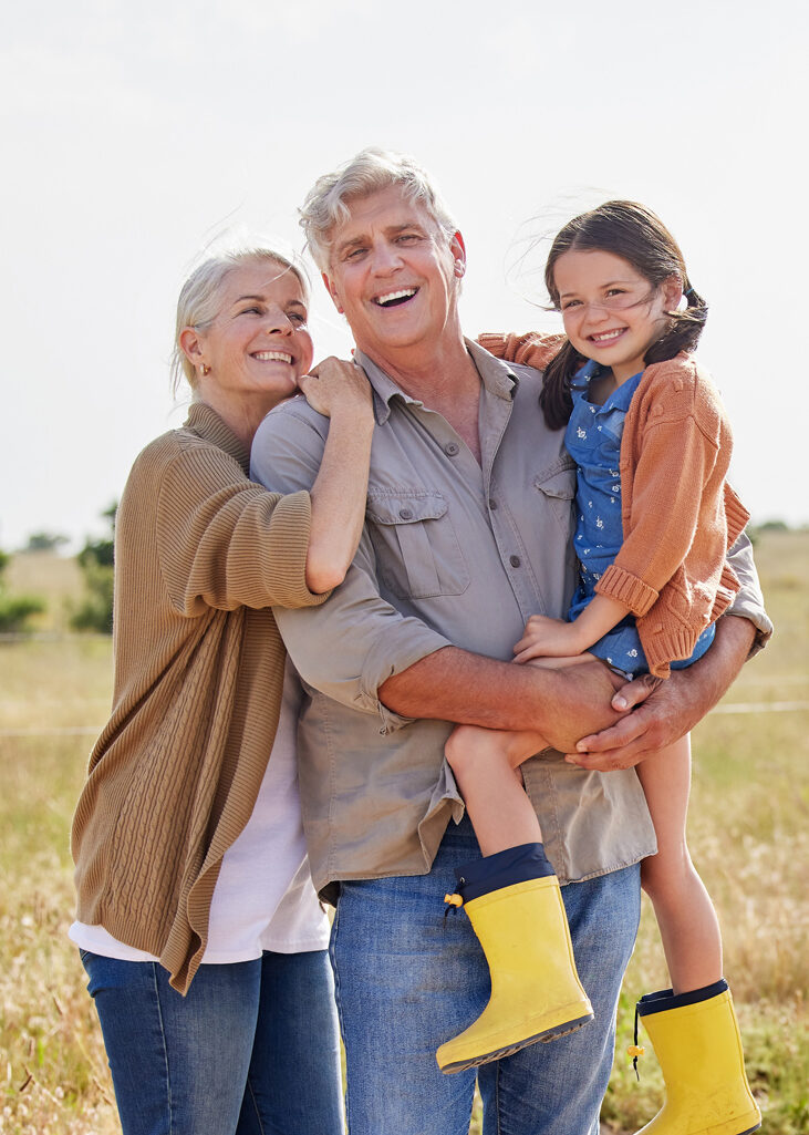 grandparents holding their granddaughter outside in a pasture