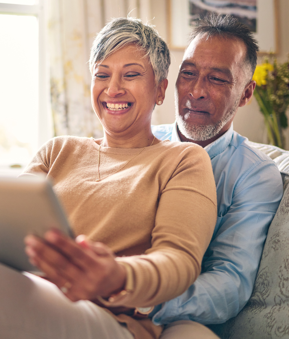 mature couple laughing together on the couch reading a tablet