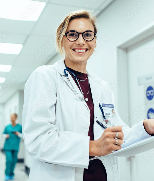 physician in hospital corridor writing on clipboard