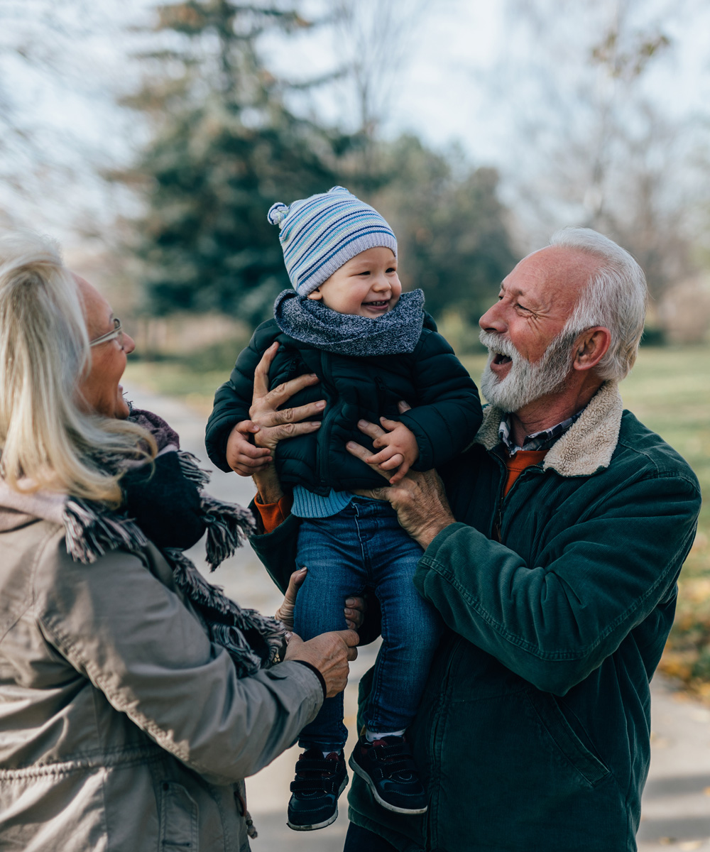 grandparents on a walk with their toddler grandson laughing and smiling