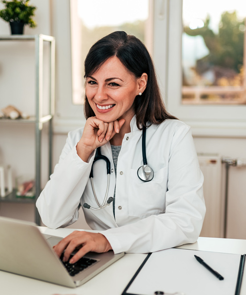 smiling female doctor sitting in front of her laptop speaking to a patient