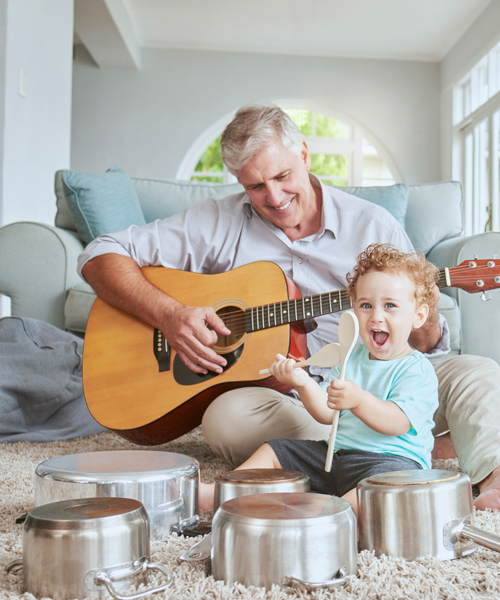 grandfather playing guitar with his toddler grandson playing drum pots from the kitchen